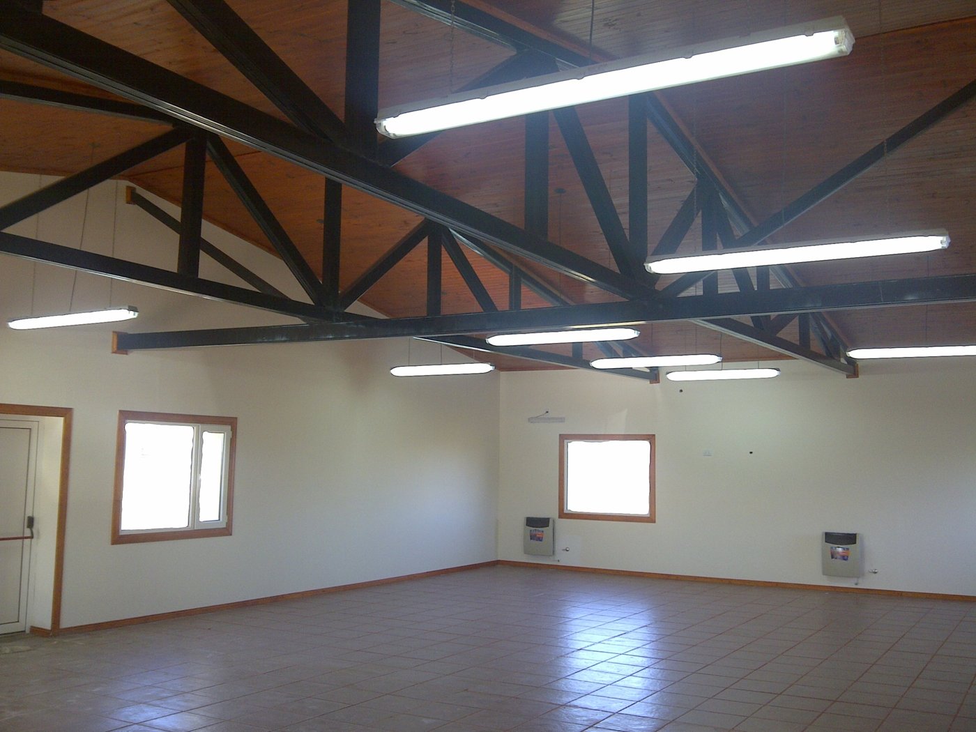 Salón terminado con cabriadas metálicas vistas e iluminación