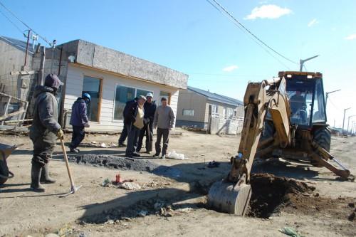 Retroexcavadora y cuadrilla trabajando frente a las viviendas