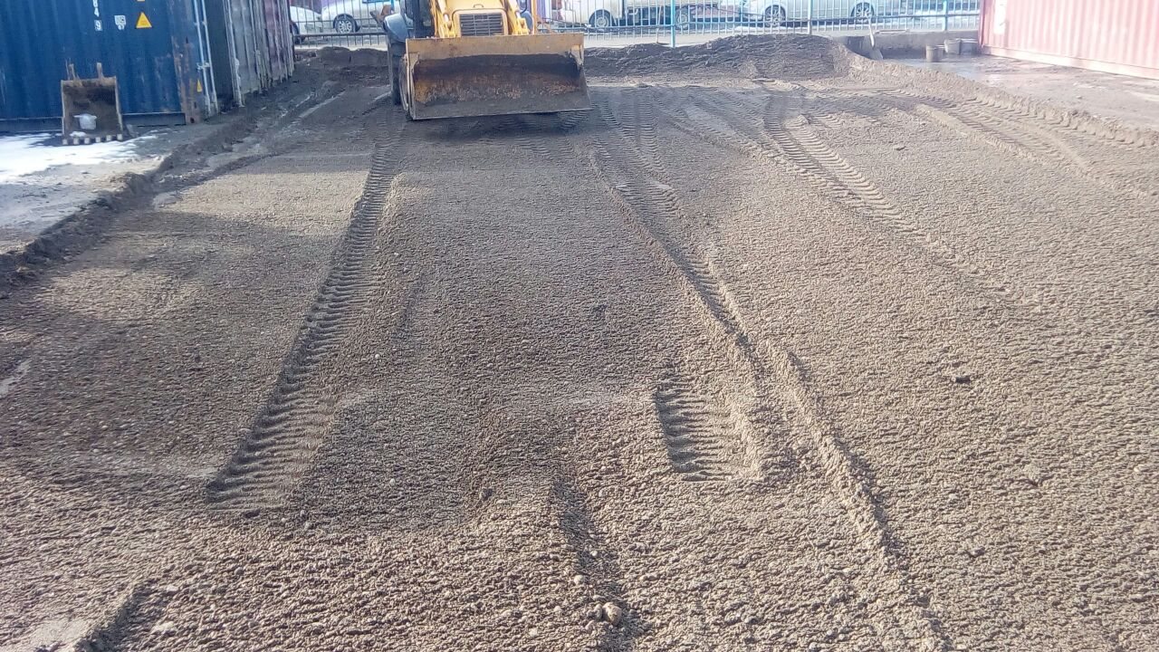 Retroexcavadora nivelando la base granular del playón