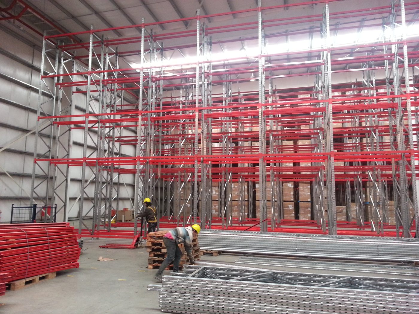 Racks rojos y galvanizados terminados con mercadería, y cuadrilla trabajando